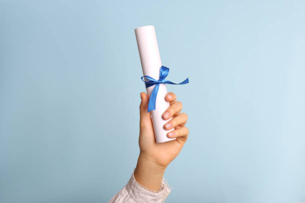 Student holding rolled diploma with ribbon on light blue background, closeup